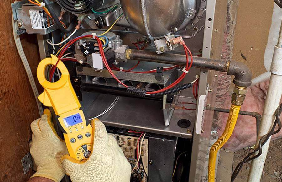 Technician using a clamp meter to test electrical components inside an HVAC unit