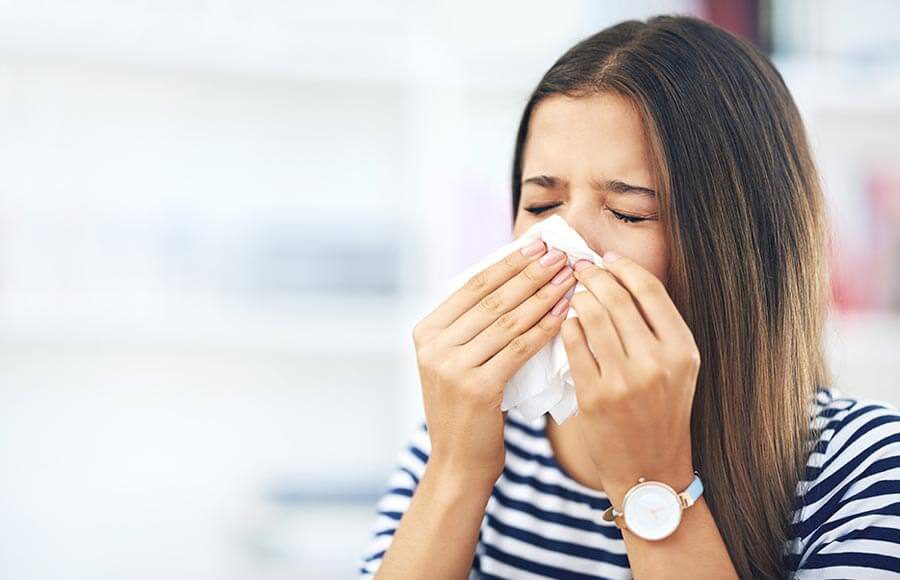 Woman blowing her nose into a tissue, appearing to suffer from allergies or a cold