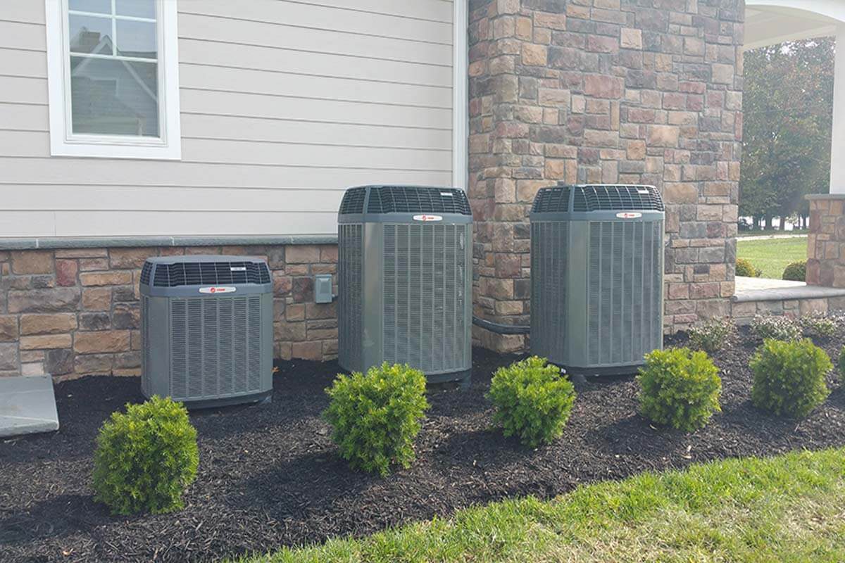 Two outdoor HVAC condenser units installed beside a brick home